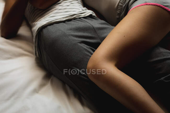 Vista lateral sección baja del hombre y la mujer disfrutando del tiempo en casa, durmiendo juntos, acostados en su cama y abrazando. - foto de stock
