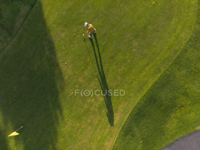 Drone shot of a man playing golf at a golf course on a sunny day, standing by a ball before taking a stroke — Stock Photo