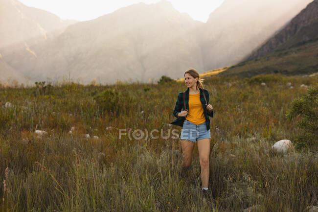 Vue de face d'une femme caucasienne s'amusant lors d'un voyage à la montagne, marchant sur un champ, par une journée ensoleillée — Photo de stock