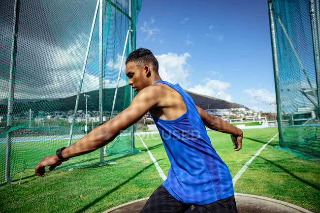 Vista laterale di un atleta maschio di razza mista che pratica in uno stadio sportivo, preparandosi a lanciare un disco. Allenamento di atletica leggera nello stadio. — Foto stock