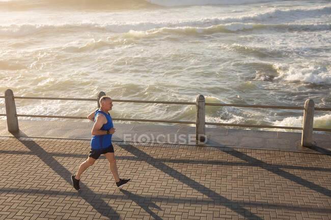 High angle side view of a mature senior Caucasian man working out on a promenade on a sunny day, running — Stock Photo