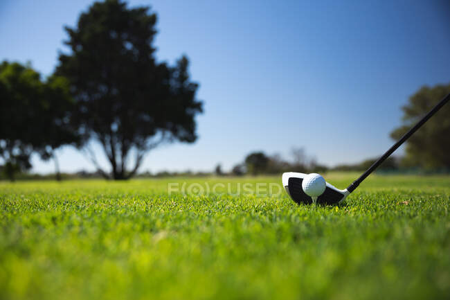 Fechar-se de um taco de golfe batendo uma bola de golfe em um tee em um campo de golfe em um dia ensolarado com céu azul — Fotografia de Stock