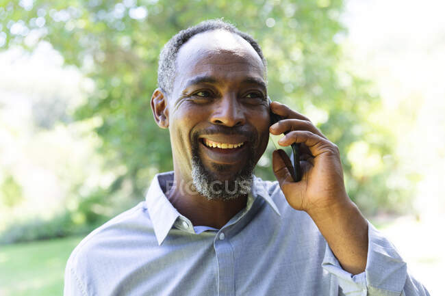 Щасливий гарний старший афроамериканець, який утішається своїм виходом на пенсію, на сонечку розмовляючи на мобільному телефоні й усміхаючись, самоізолюючись під час коронавірусної угоди 19 - річної пандемії — стокове фото