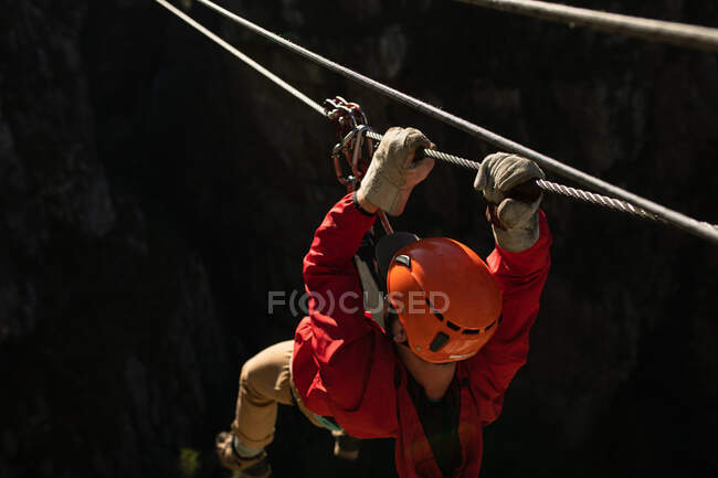 Rear view of Caucasian man enjoying time in nature, zip lining, holding the rope, on a sunny day in mountains — Stock Photo