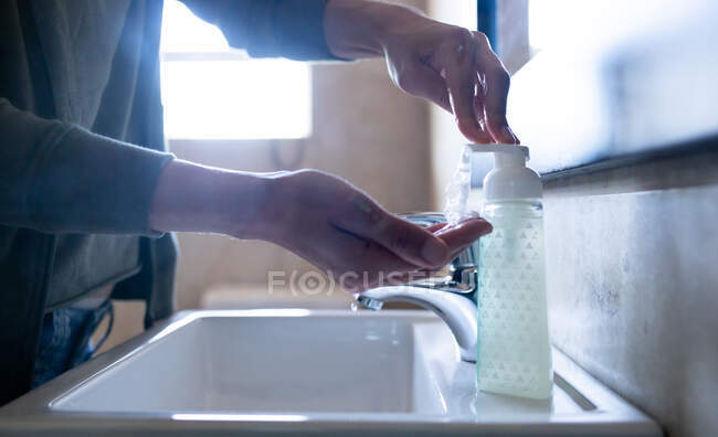 Primer plano de las manos de la mujer en casa en el baño durante el día lavándose las manos en un lavabo con jabón líquido, protección contra la infección por coronavirus Covid-19 y pandemia. Distanciamiento social y autoaislamiento en cuarentena - foto de stock