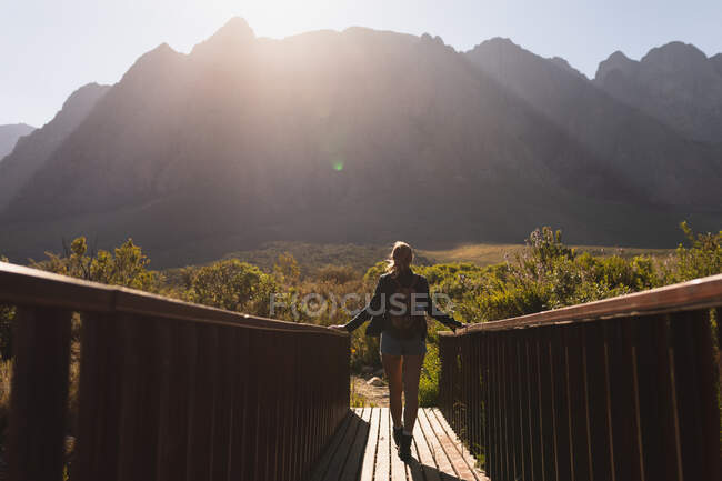 Visão traseira de uma mulher caucasiana se divertindo em uma viagem às montanhas, de pé em uma ponte, apreciando sua vista, em um dia ensolarado — Fotografia de Stock