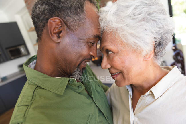 Primo piano di felice anziano pensionato coppia afroamericana a casa in piedi nella loro cucina, toccando la testa insieme, guardandosi e sorridendo mentre abbraccia, a casa insieme isolando durante il coronavirus covid19 pandemia — Foto stock