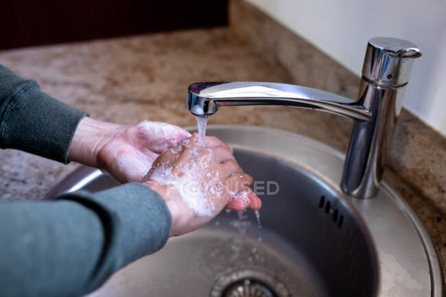 Primo piano di una mano di donna a casa in bagno durante il giorno lavarsi le mani in un lavandino, utilizzando sapone, protezione contro l'infezione coronavirus Covid-19 e pandemia. Distanziamento sociale e autoisolamento in quarantena — Foto stock