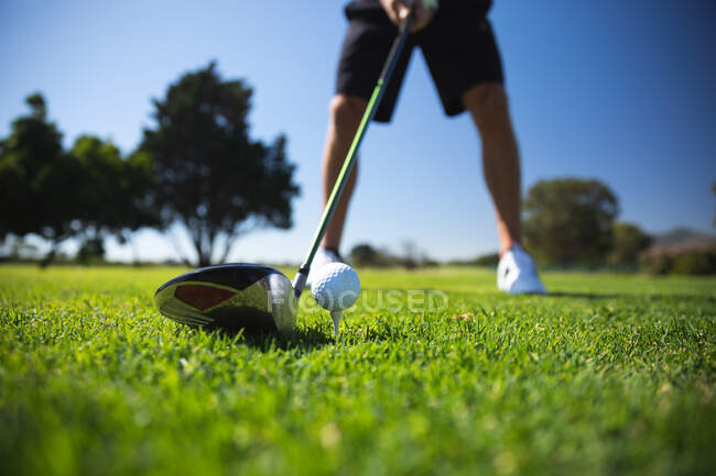 Низкая часть человека на поле для гольфа в солнечный день с голубым небом, готовясь ударить по мячу клюшкой для гольфа — стоковое фото