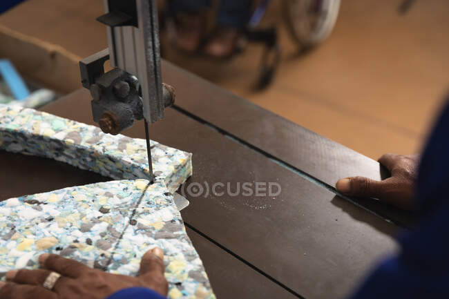 Close-up do trabalhador masculino em uma oficina em uma fábrica de fazer cadeiras de rodas, de pé em uma bancada, folhas de corte de espuma com uma ferramenta elétrica — Fotografia de Stock
