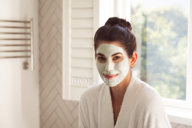 Portrait de femme métisse passant du temps à la maison, avec masque dans la salle de bain. Auto-isolement et distanciation sociale en quarantaine pendant l'épidémie de coronavirus covid 19. — Photo de stock