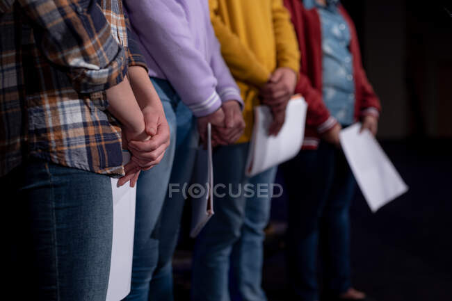 Вид збоку середня секція групи підлітків-чоловіків і жінок-хореографів, що стоять в ряд, тримаючи ноти на сцені шкільного театру під час репетицій для виступу — стокове фото