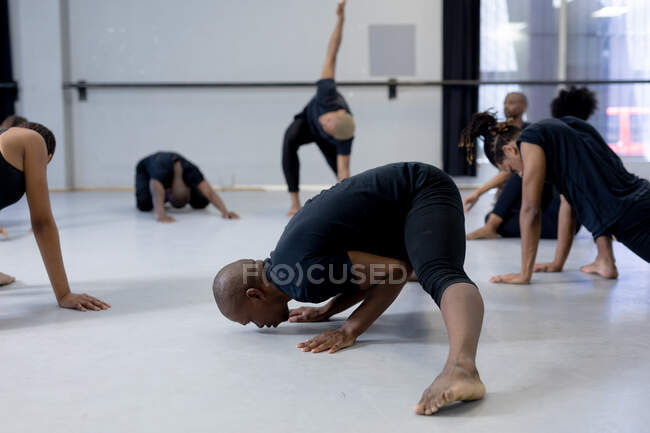 Side view of a multi-ethnic group of fit male and female modern dancers wearing black outfits practicing a dance routine during a dance class in a bright studio, creating a circle and stretching up. — Stock Photo