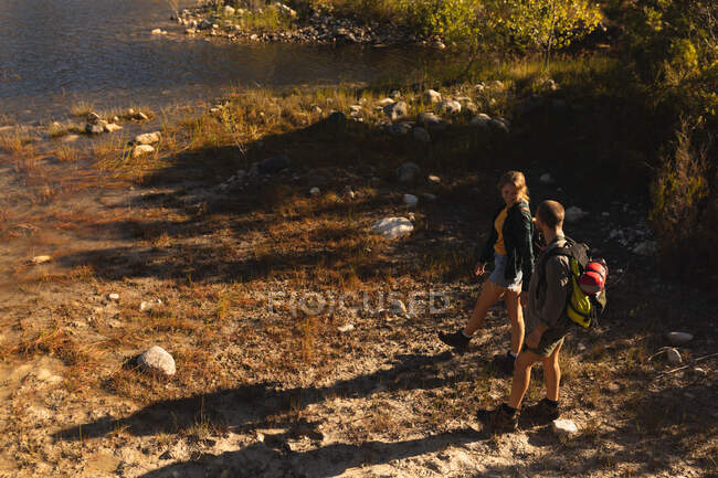 Vista de alto ângulo de um casal caucasiano se divertindo em uma viagem às montanhas, andando em uma costa, de mãos dadas, olhando um para o outro, em um dia ensolarado — Fotografia de Stock