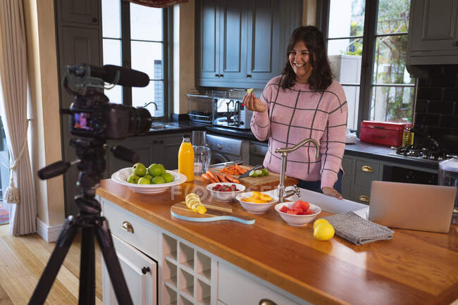 Caucasian female vlogger at home in her kitchen, demonstrating preparing food recipes in front of a camera for her online blog. Social distancing and self isolation in quarantine lockdown. — Stock Photo