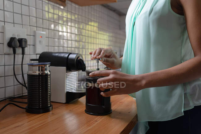 Вид сбоку: женщина дома, стоящая на кухне, готовит кофе в кафе. — стоковое фото
