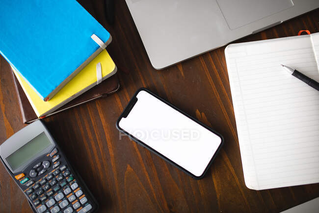 Overhead view of notebooks, a smartphone, an open book, a pen, a calculator and a laptop computer on a wooden table at home — Stock Photo