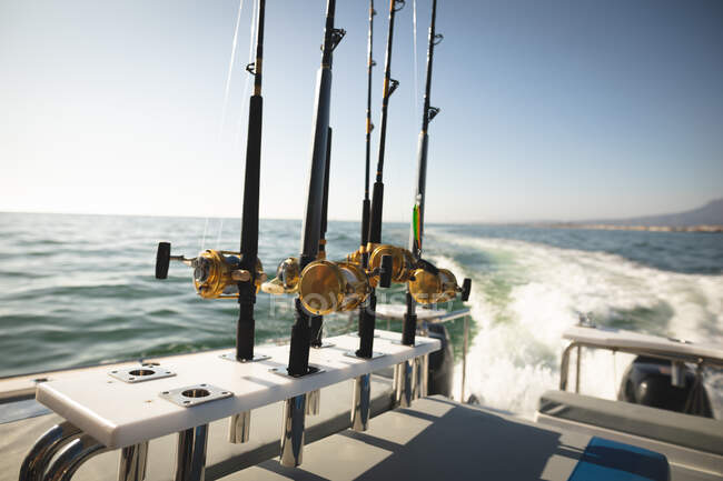 Cañas de pescar de pie en un barco, listas para ser utilizadas, en un día soleado, con el mar en el fondo - foto de stock
