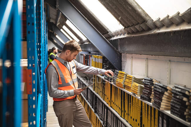 Two Caucasian male factory workers wearing a high vis vest checking stock and holding clipboard. Workers in industry at a factory making hydraulic equipment. — Stock Photo