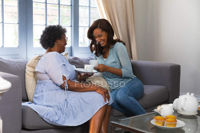 Femme de race mixte senior passant du temps à la maison avec sa fille, distanciation sociale et isolement personnel en quarantaine, prendre le thé ensemble et parler — Photo de stock