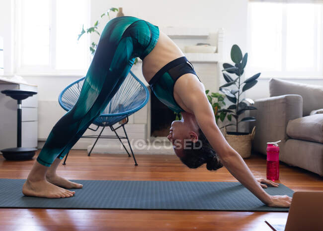 Kaukasische Frau verbringt Zeit zu Hause, trägt Sportbekleidung, sitzt auf einer Yogamatte und streckt sich, nimmt mit ihrem Laptop am Online-Yoga-Kurs teil. Soziale Distanzierung und Selbstisolierung in Quarantäne. — Stockfoto