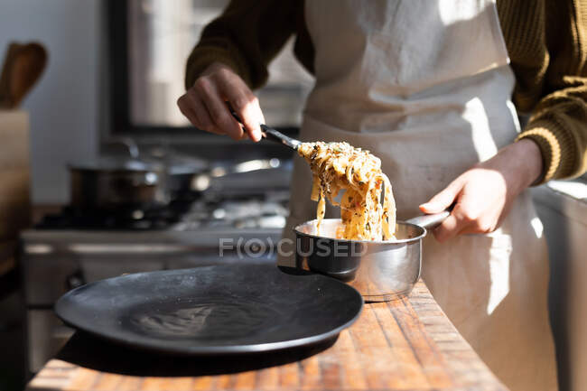 Mid section of woman wearing an apron, putting pasta on a plate. Social distancing and self isolation in quarantine lockdown. — Stock Photo