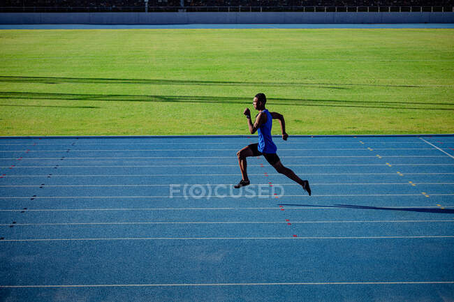 Vista lateral de un atleta masculino de raza mixta practicando en un estadio deportivo, corriendo. - foto de stock
