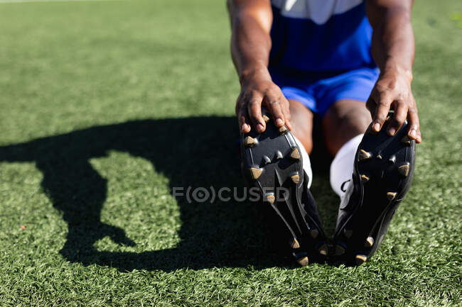 Jogador de futebol vestindo um treinamento de tira de equipe em um campo de esportes ao sol, aquecendo-se esticando as pernas . — Fotografia de Stock