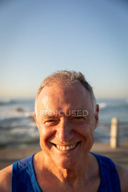 Retrato de cerca de un hombre caucásico mayor maduro disfrutando haciendo ejercicio en un paseo marítimo en un día soleado con cielo azul, sonriendo a la cámara - foto de stock