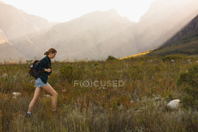Vista lateral de uma mulher caucasiana se divertindo em uma viagem às montanhas, andando em um campo, em um dia ensolarado — Fotografia de Stock
