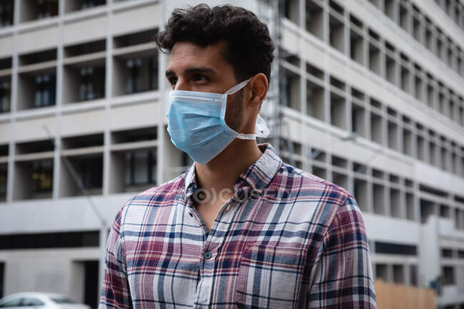 Vue de face gros plan d'un homme caucasien portant une chemise à carreaux et un masque facial contre la pollution atmosphérique et le coronavirus covid19, marchant dans les rues de la ville. — Photo de stock