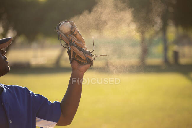Вид сбоку крупным планом на бейсболиста смешанной расы во время игры в бейсбол в солнечный день, ловящего мяч своей перчаткой — стоковое фото