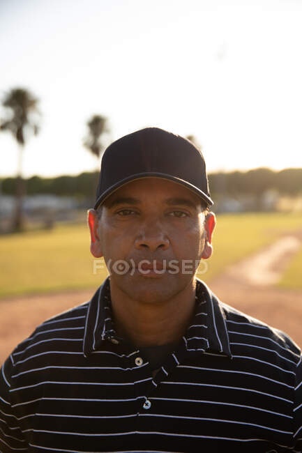 Ritratto di un arbitro di baseball maschile di razza mista, in uniforme e cappello, in piedi su un campo da baseball, che guarda una telecamera — Foto stock
