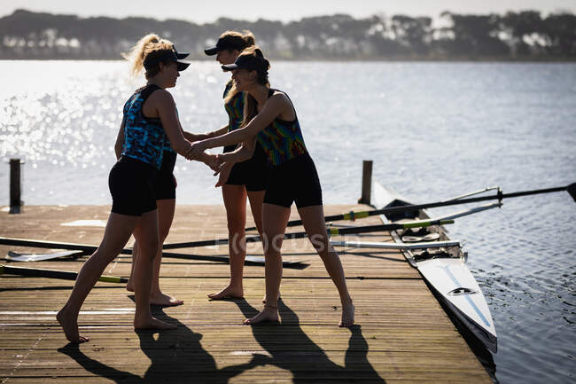 Біля входу в веслувальну групу з чотирьох кавказьких жінок, які тренуються на річці, стоять на пристані на сонці, трясучи руки і розмовляючи перед веслуванням. — стокове фото