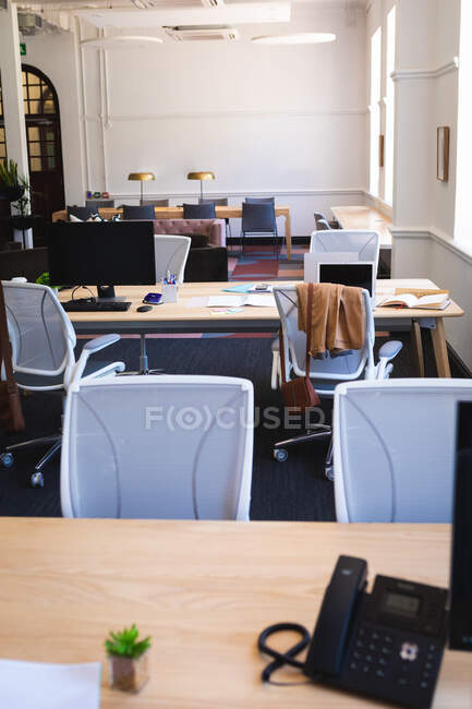 Общий вид пустого современного офиса с настольными компьютерами, лежащими на столах, с телефоном на переднем плане, в солнечный день — стоковое фото