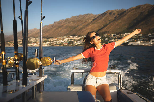 Ein junges kaukasisches Mädchen genießt die Zeit in der Sonne an der Küste, auf einem Boot stehend, mit ausgestreckten Armen — Stockfoto