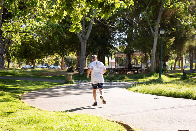 Vista trasera de un atlético hombre mayor caucásico haciendo ejercicio en un parque en un día soleado, corriendo en una pista - foto de stock