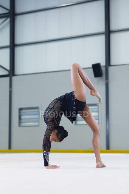 Вид сбоку на юношескую смешанную расовую гимнастку, выступающую в спортзале, сгибающуюся назад, с руками на полу, в черном трико — стоковое фото