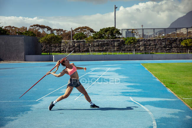 Side view of a Caucasian female athlete practicing at a sports stadium, throwing a javelin. — Stock Photo