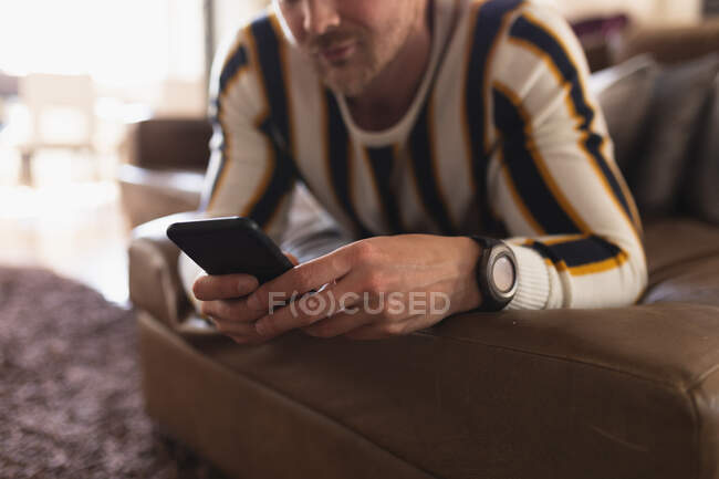 Vista frontale da vicino di un giovane caucasico che trascorre del tempo a casa, sdraiato su un divano e usando il suo smartphone. — Foto stock