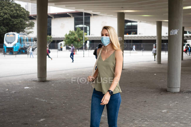 Front view of a caucasian woman out and about in the city streets during the day, wearing face mask against air pollution and covid19 coronavirus. — Stock Photo