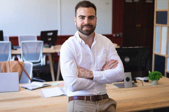 Portrait of a Caucasian businessman wearing a white shirt, working in a modern office, standing and smiling, looking at camera with arms crossed — Stock Photo