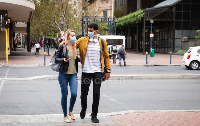 Vue de face d'un couple caucasien dans les rues de la ville pendant la journée, portant des masques faciaux contre la pollution atmosphérique et le coronavirus covid19. — Photo de stock