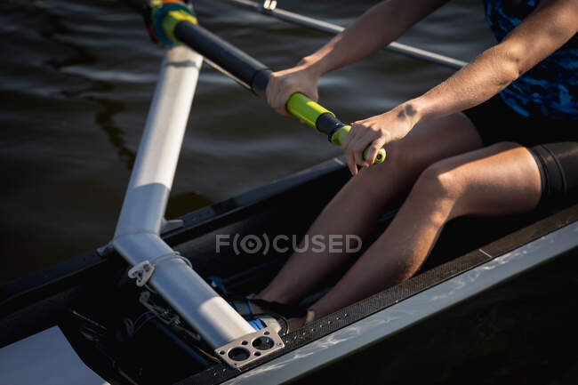 Низкий вид сбоку секции женщины от гребной команды тренировки на реке, гребля в гоночной раковине на воде на солнце — стоковое фото