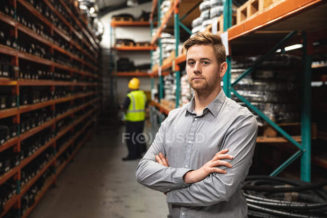 Portrait of a Caucasian male factory supervisor looking at camera with arms crossed, with workers in the background. Workers in industry at a factory making hydraulic equipment. — Stock Photo