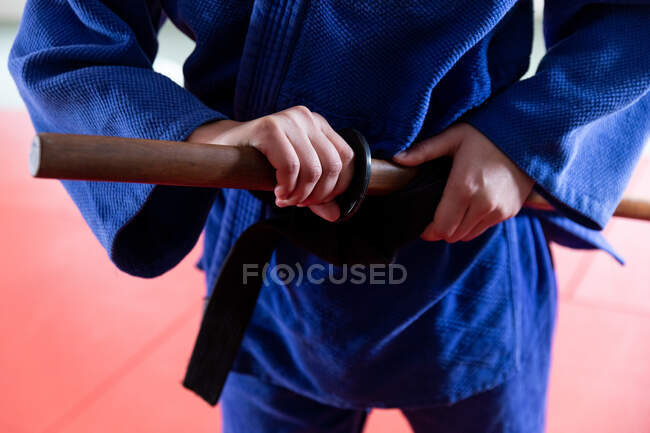 Vue de face de la section médiane du judoka portant du judogi bleu, tenant du judo jo stick en bois, debout dans la salle de gym pendant un entraînement de judo. — Photo de stock