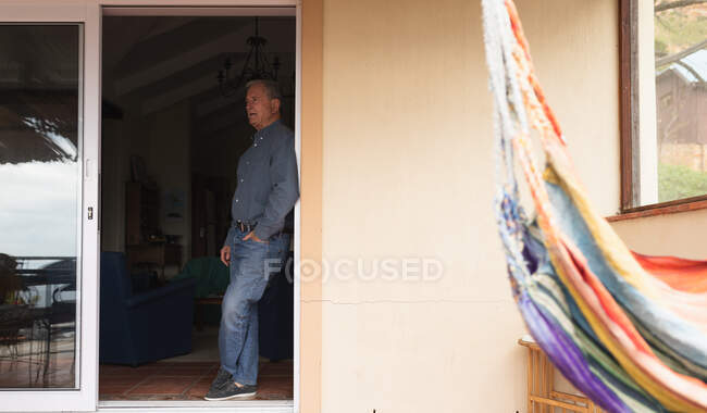 Vista laterale di un anziano caucasico che si rilassa a casa, in piedi in una porta aperta, appoggiato e pensando, ammirando la vista — Foto stock