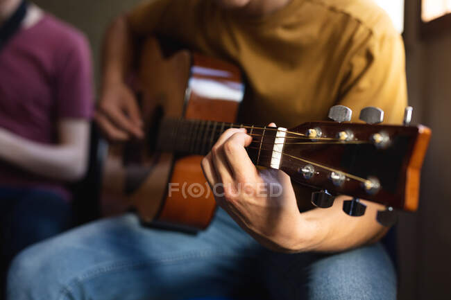 Front view mid section of musician teenage boy sitting and playing an acoustic guitar. Shot in music school. — Stock Photo
