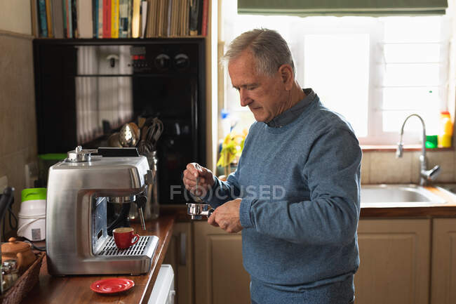 Vista laterale di un anziano caucasico che si rilassa a casa, prepara il caffè da usare in una macchina da caffè espresso, in piedi nella sua cucina — Foto stock