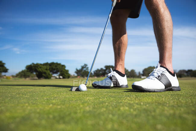 Section basse de l'homme sur un terrain de golf par une journée ensoleillée avec ciel bleu, se préparant à frapper une balle de golf — Photo de stock